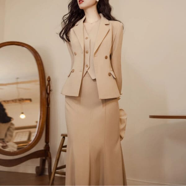 A woman in a beige suit standing next to a mirror.