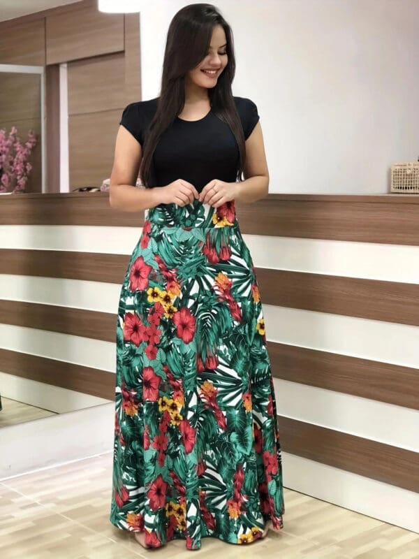 A woman standing in front of a wall wearing a black top and floral skirt.