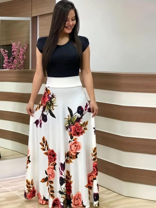 A woman standing in front of a wall wearing a black top and floral skirt.