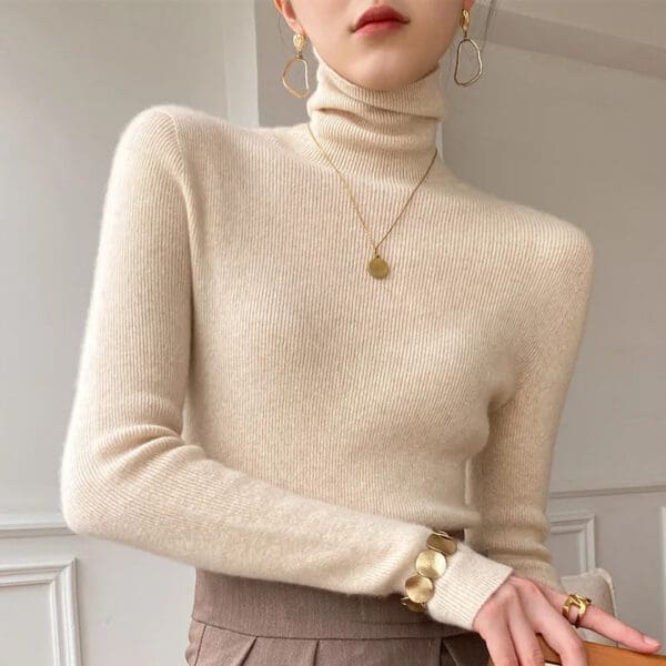 A woman wearing a beige sweater and holding her hand in the other.