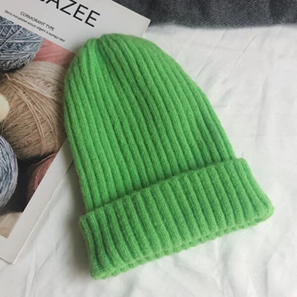 A green beanie is sitting on top of a bed.