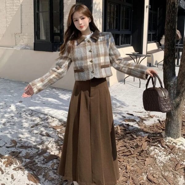 A woman in brown skirt and plaid jacket holding a purse.