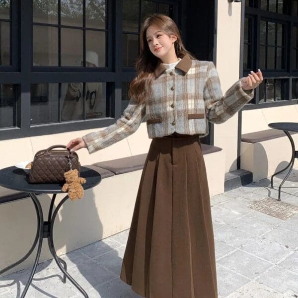 A woman in brown skirt and plaid shirt standing next to table.