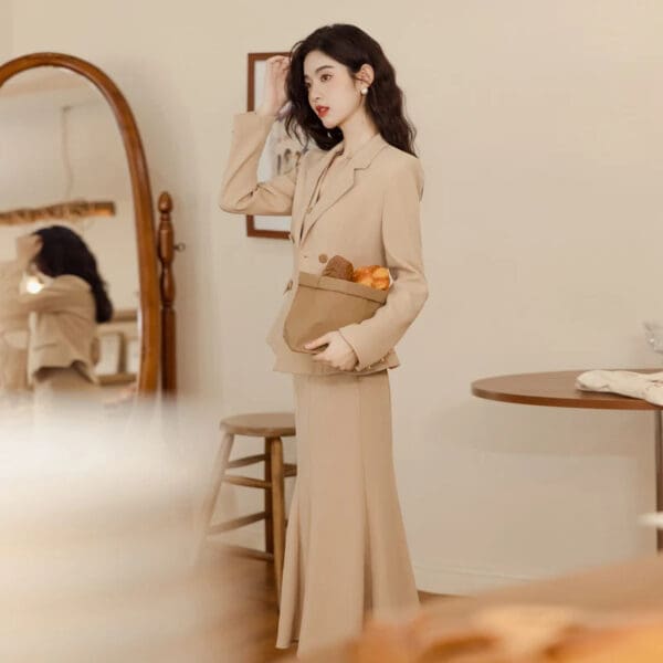 A woman in beige dress standing next to a mirror.