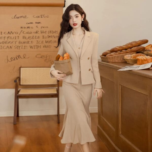 A woman in a tan suit holding a box of pastries.