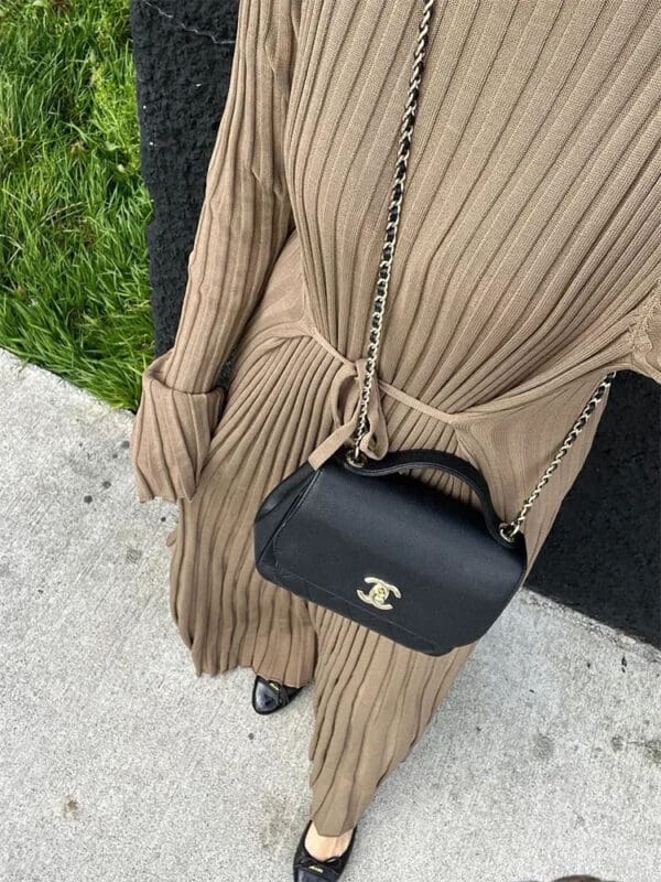 A woman in a tan dress holding a black purse.