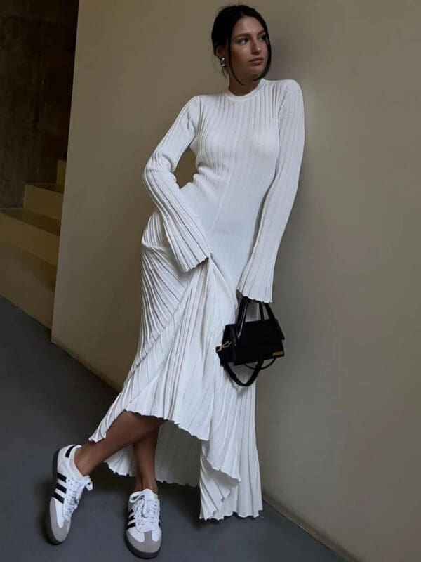 A woman in white dress leaning on wall.