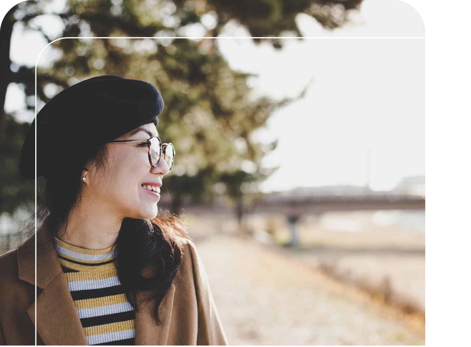 A woman wearing glasses and a hat is smiling.